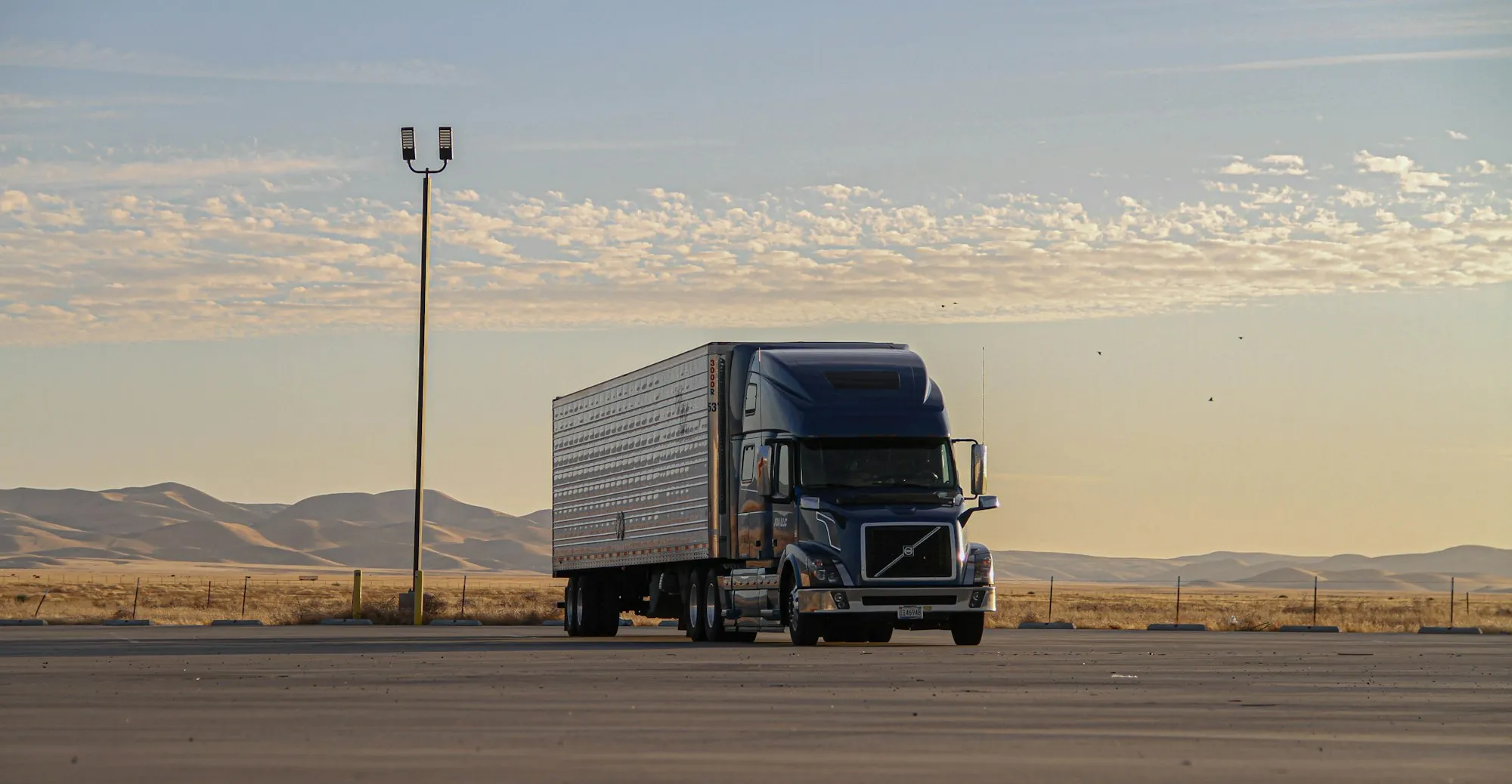 A semi truck parked under a wide desert dawn sky, mountains on the horizon