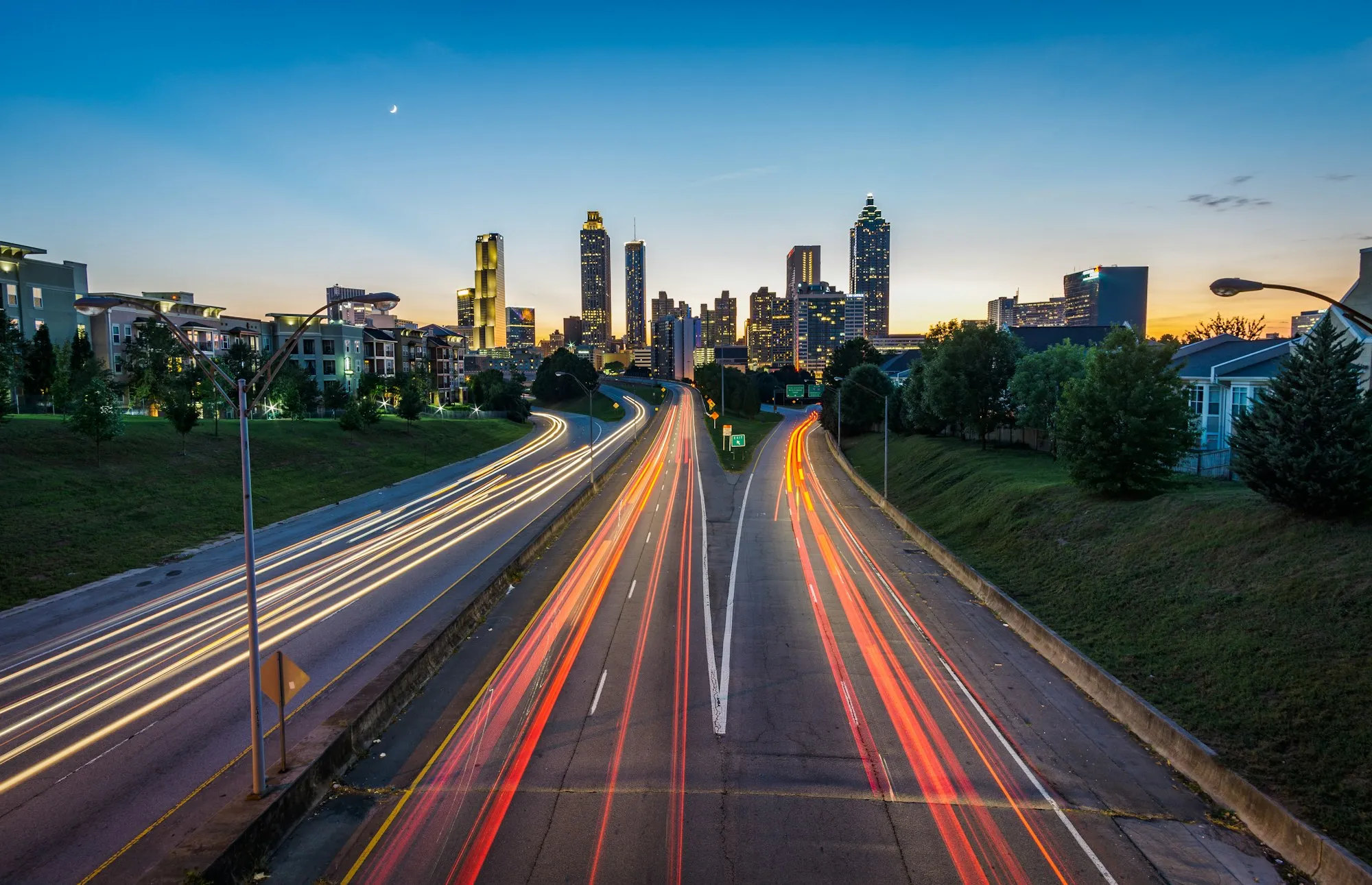 Light trails streaking down a highway toward a city skyline at dusk
